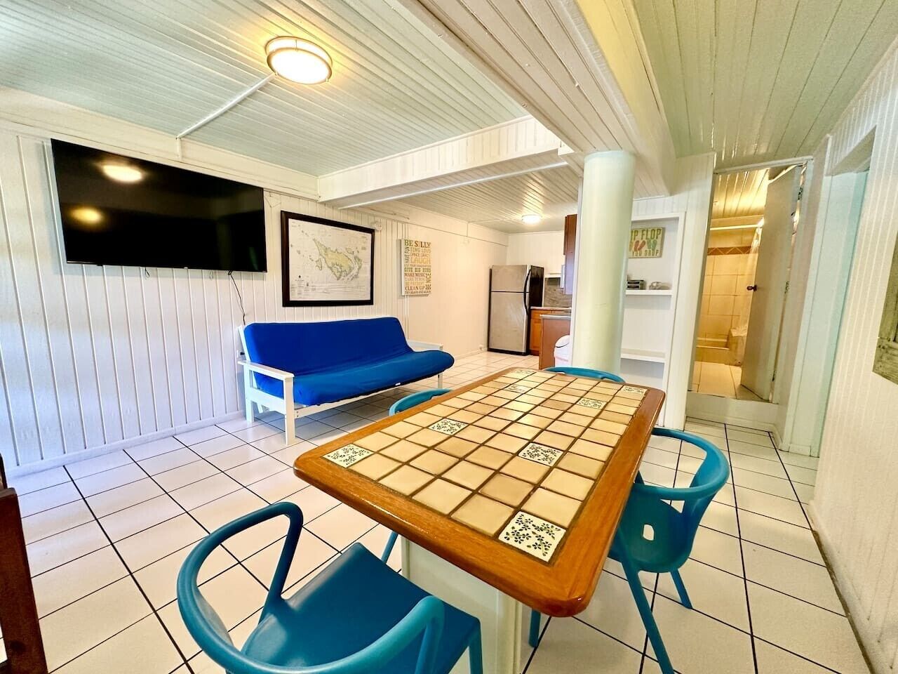 Une pièce avec une table à carreaux, des chaises bleues, un canapé bleu et un téléviseur accroché au mur.