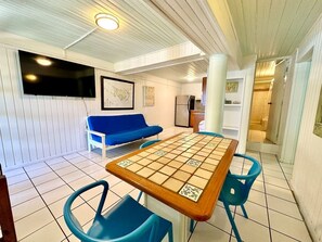 Una habitación con una mesa a cuadros, sillas azules, un sofá azul y un televisor en la pared.