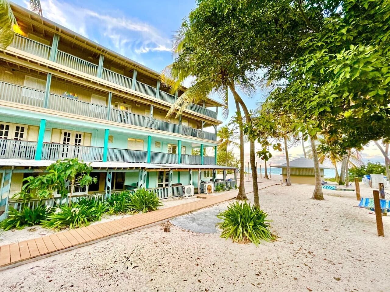 A multi-story hotel with balconies, a sandy beach area, and tropical vegetation.