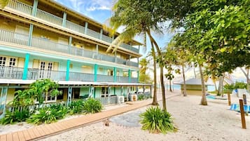 A multi-story hotel with balconies, a sandy beach area, and tropical vegetation.