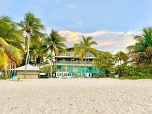 Ein Strandhotel mit mehreren Balkonen, Palmen und einem Sandstrand.