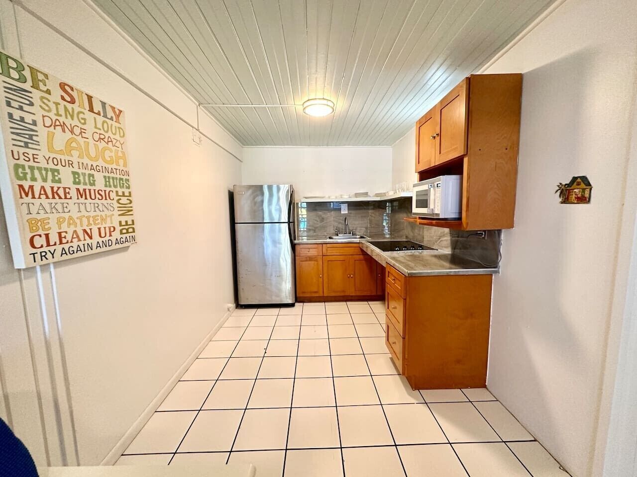 Cocina compacta con gabinetes de madera, un refrigerador de acero inoxidable y un microondas.