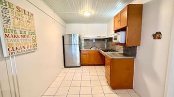 Cocina compacta con gabinetes de madera, un refrigerador de acero inoxidable y un microondas.