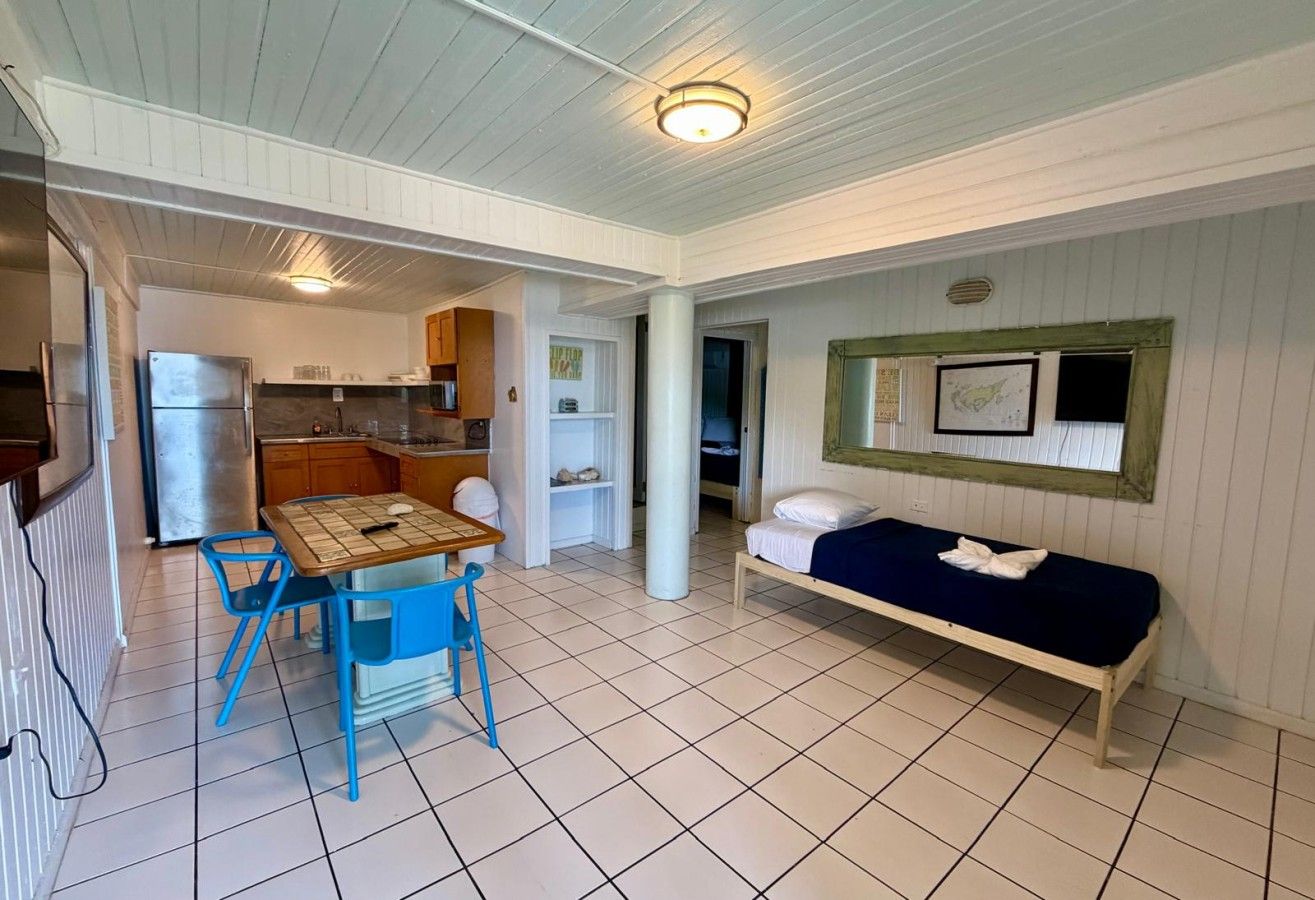 A compact room with a kitchenette, a dining table with chairs, a bed, and a small window.