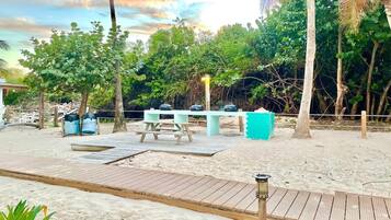 Ein Strandbereich mit Sand, einer Holzterrasse, Picknicktischen und einem Grill.