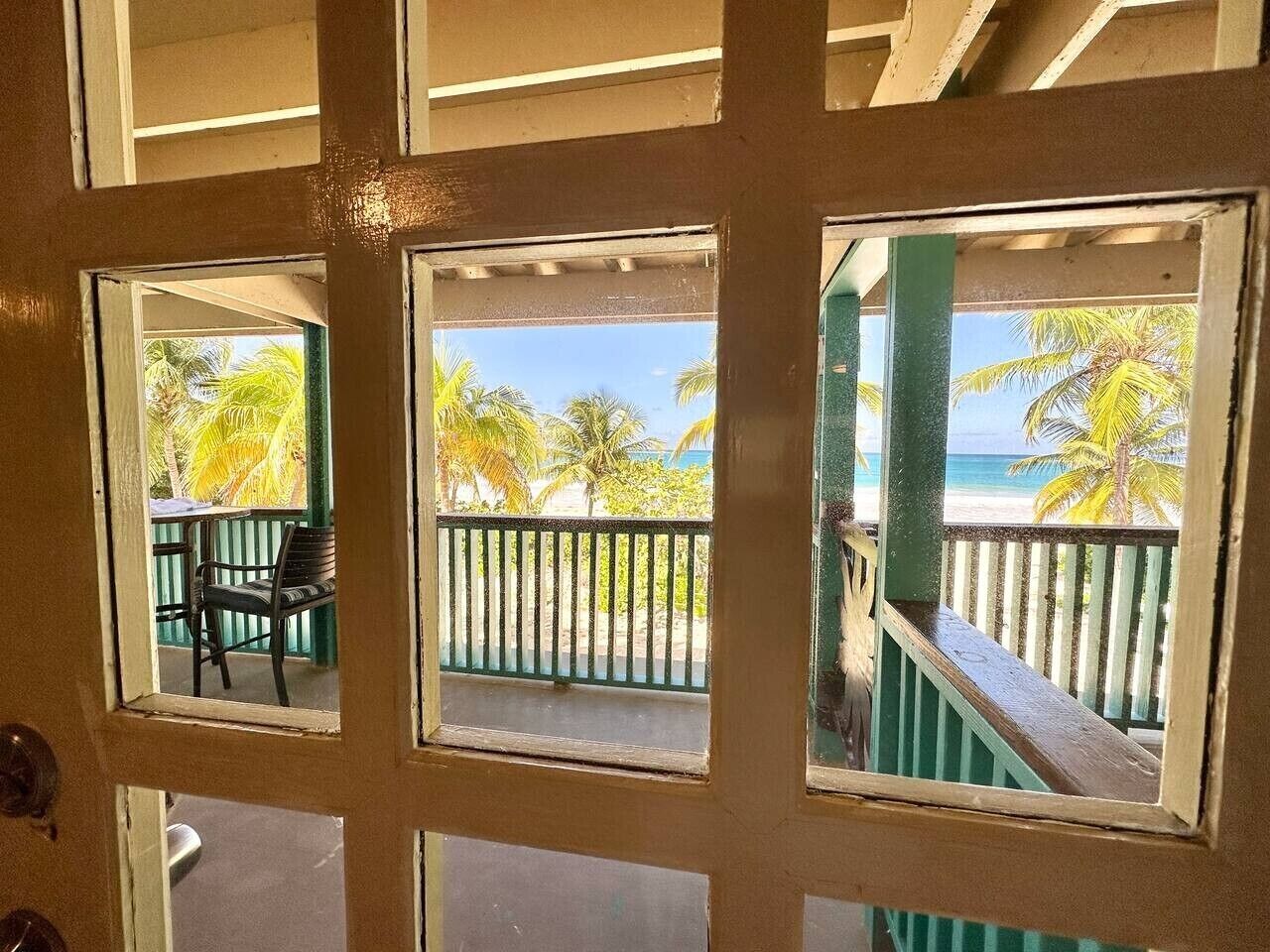 A door with three windows, each offering a view of a beach with palm trees and a clear sky.