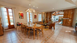 A spacious dining area with a wooden table and chairs, a chandelier, and a view of a pool through a glass door. - Casa Vama Pool Private Cinema (Amelie-les-Bains-Palalda)