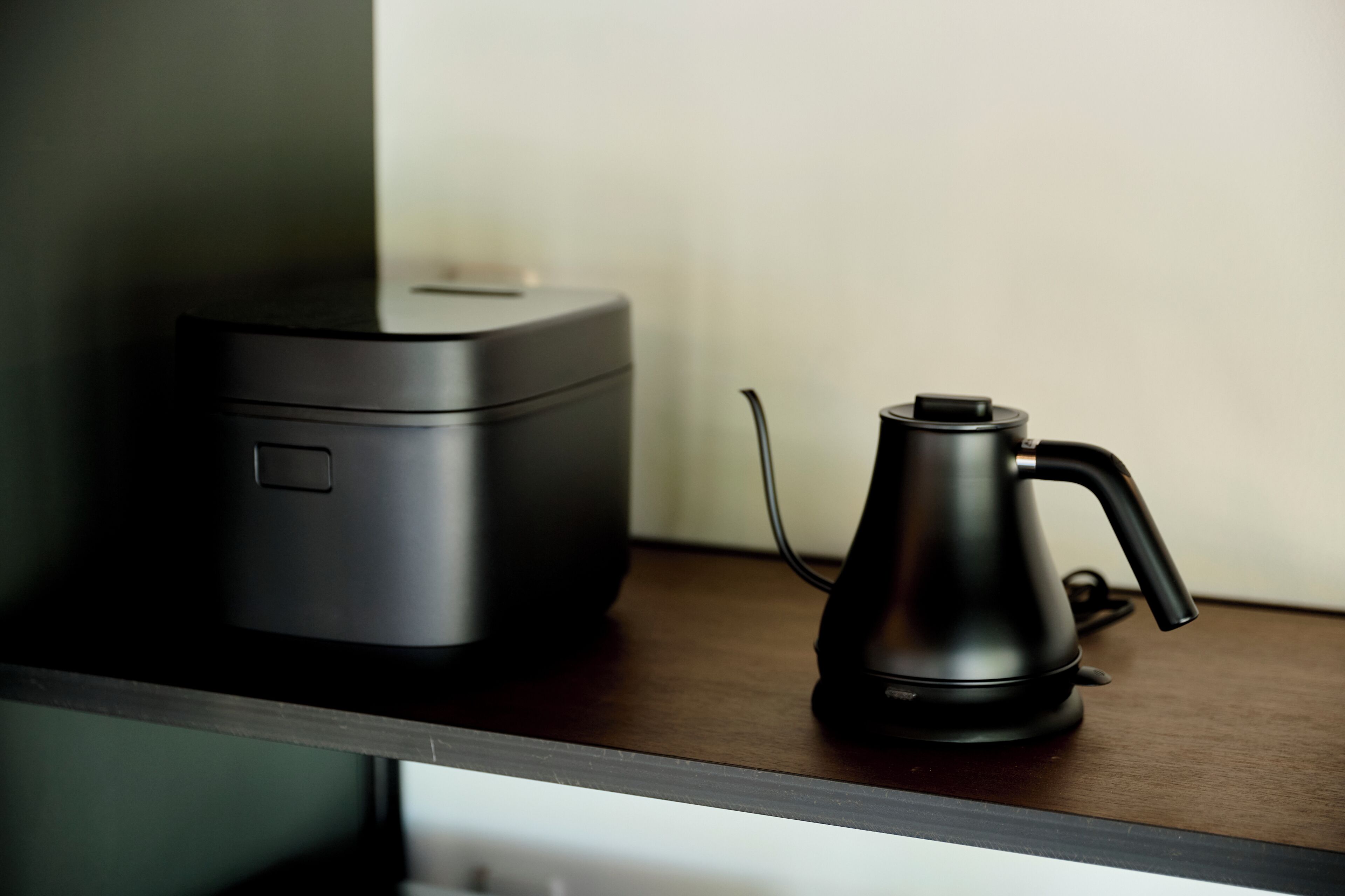 Eine Kaffeemaschine und ein schwarzes Gerät auf einer Holztischplatte.