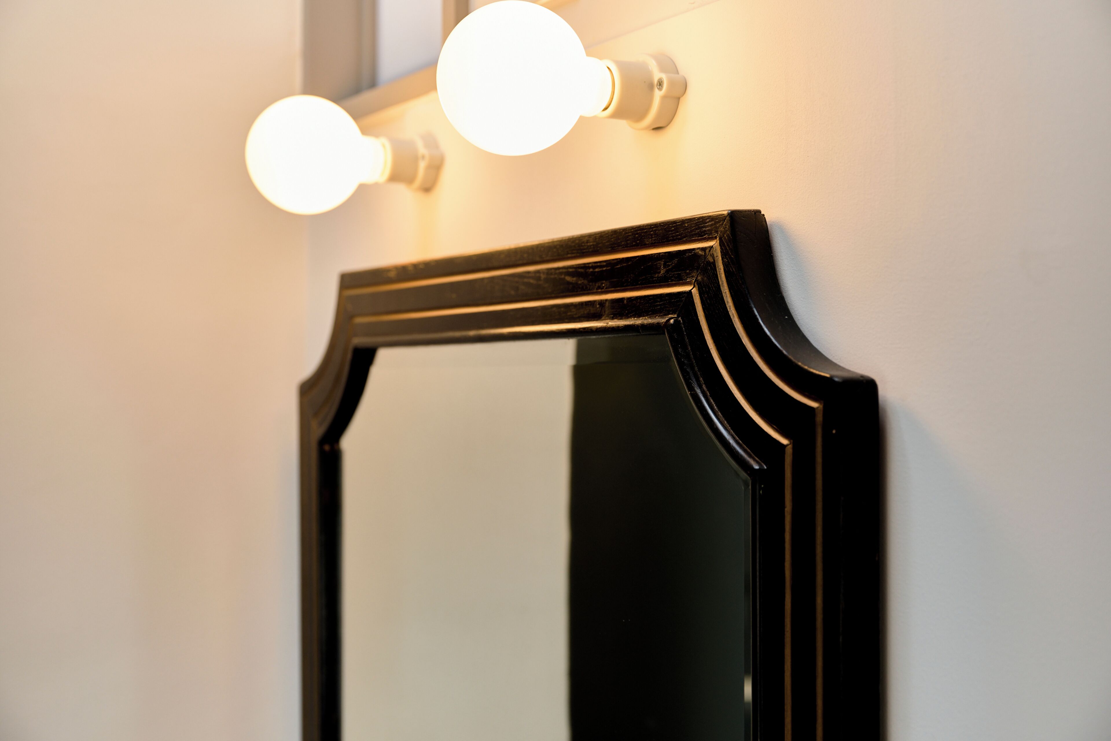 A mirror with a black frame and two round lights above it.