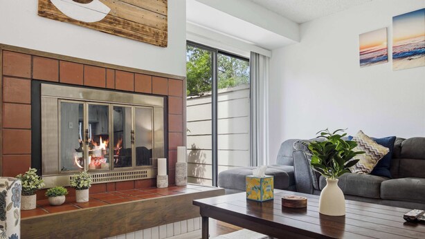 A living room with a fireplace, a sofa, a coffee table, and a large window. - Townie at the Foothills | Hop, Skip & Hike (Fort Collins)