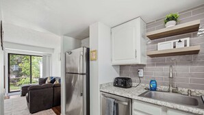 A modern kitchen with a stainless steel refrigerator, a granite countertop, and a built-in dishwasher. - Townie at the Foothills | Hop, Skip & Hike (Fort Collins)