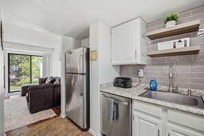 A modern kitchen with a stainless steel refrigerator, a granite countertop, and a built-in dishwasher. - Townie at the Foothills | Hop, Skip & Hike (Fort Collins)