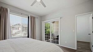 Un dormitorio con cama, ventilador de techo, puerta corrediza al balcón y una puerta blanca.