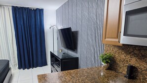 A compact kitchen with a granite countertop, a microwave, a small plant, and a TV on a stand. - Beautiful Oceanfront Studio in Marco Polo Sunny Isles Beach (Sunny Isles Beach)