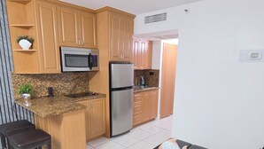 A kitchen with wooden cabinets, a stainless steel refrigerator, a microwave, and a granite countertop. - Beautiful Oceanfront Studio in Marco Polo Sunny Isles Beach (Sunny Isles Beach)