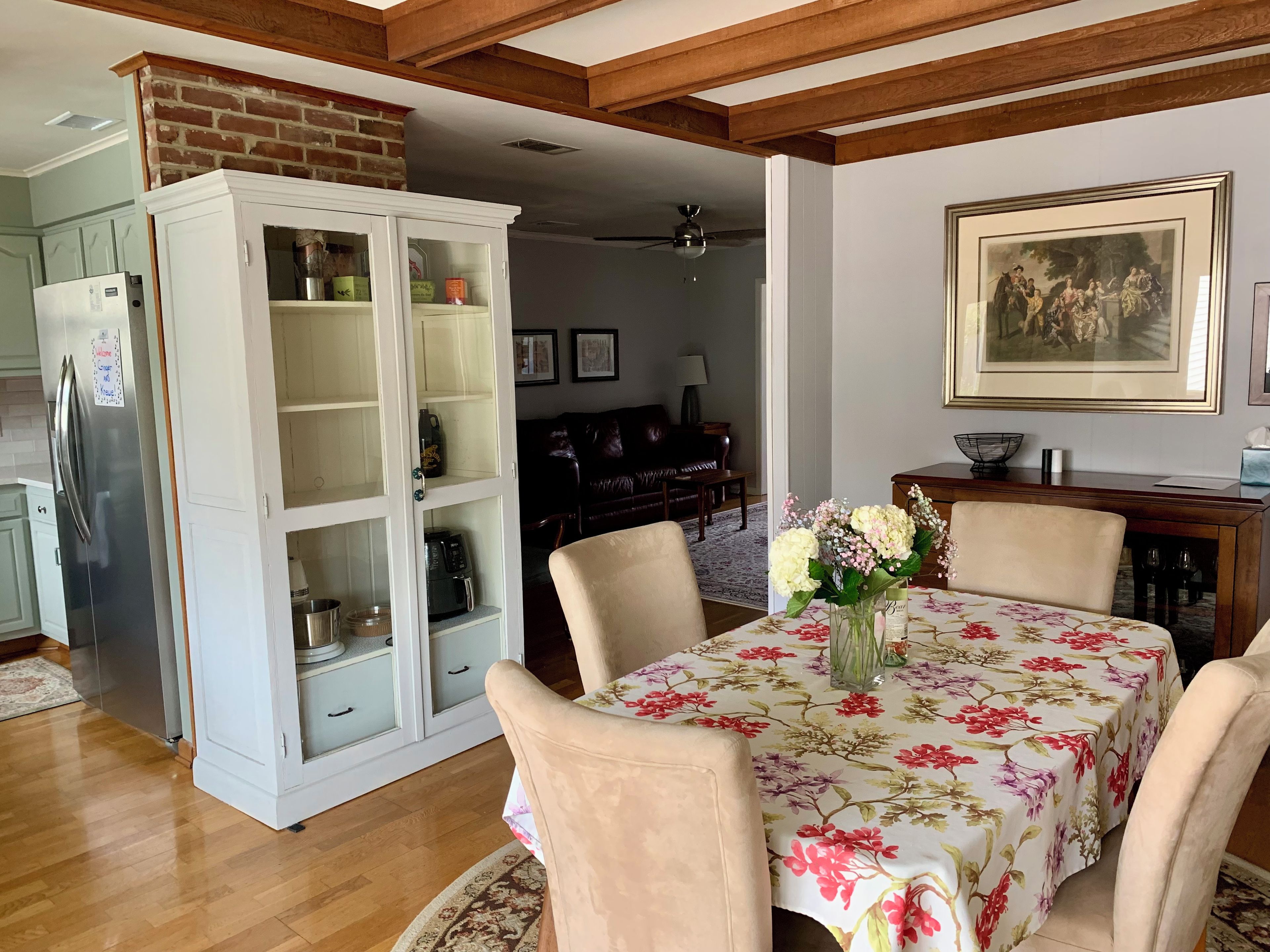 Un coin repas avec une table dressée pour quatre personnes, entourée de chaises, un meuble avec des portes en verre et un réfrigérateur.