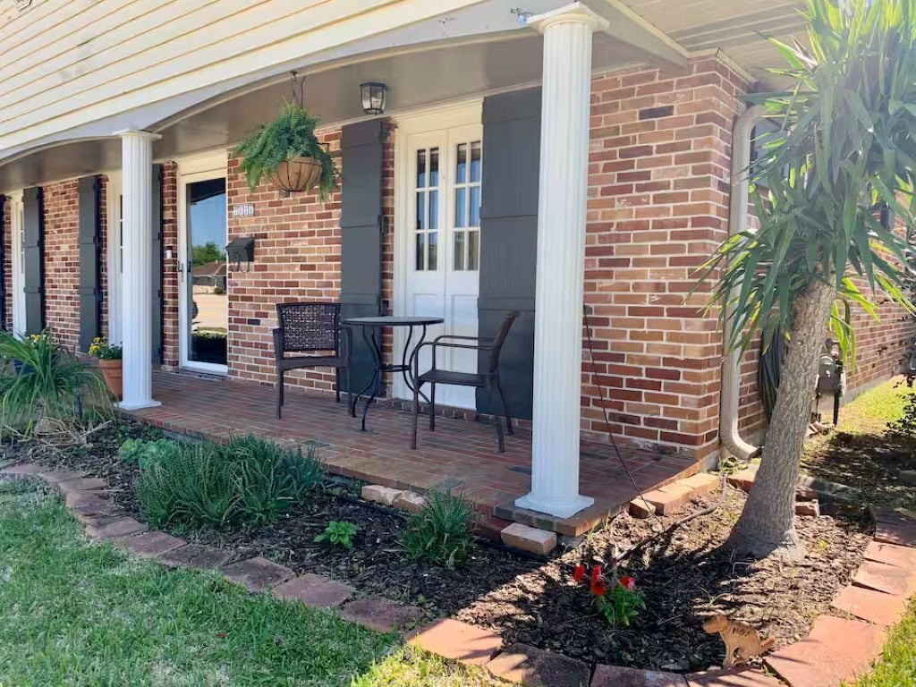 A brick building with a covered porch, outdoor seating, and a garden area.