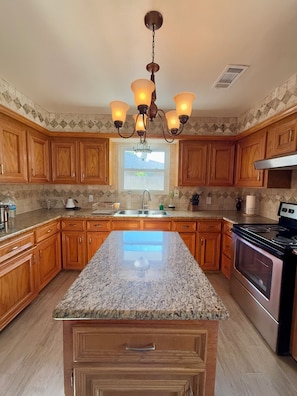 A kitchen with wooden cabinets, granite countertops, a stainless steel stove, and a chandelier. - Cozy & Charming Stay Min from Hobby, NRG, Downtown, NASA (Houston)