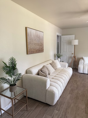 A living room with a beige sofa, a glass coffee table, a potted plant, a floor lamp, and a door. - Cozy & Charming Stay Min from Hobby, NRG, Downtown, NASA (Houston)