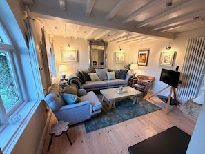 En stue med sofa, lænestol, sofabord, fjernsyn og billeder på væggene.