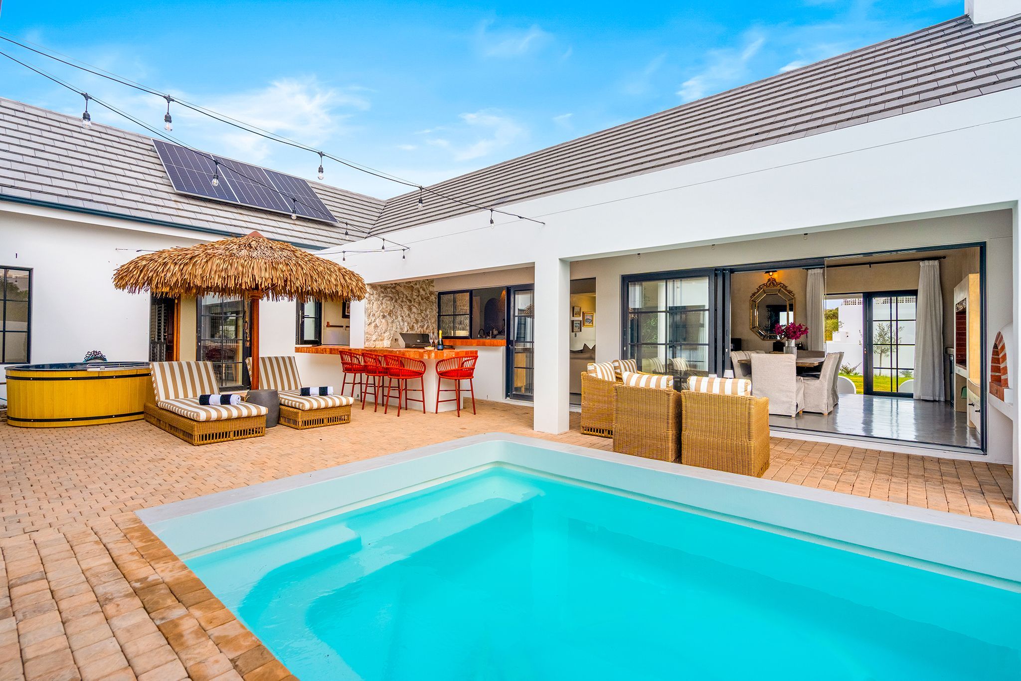 Ein moderner Poolbereich im Freien mit Whirlpool, Liegestühlen und Essbereich mit Tisch und Stühlen.