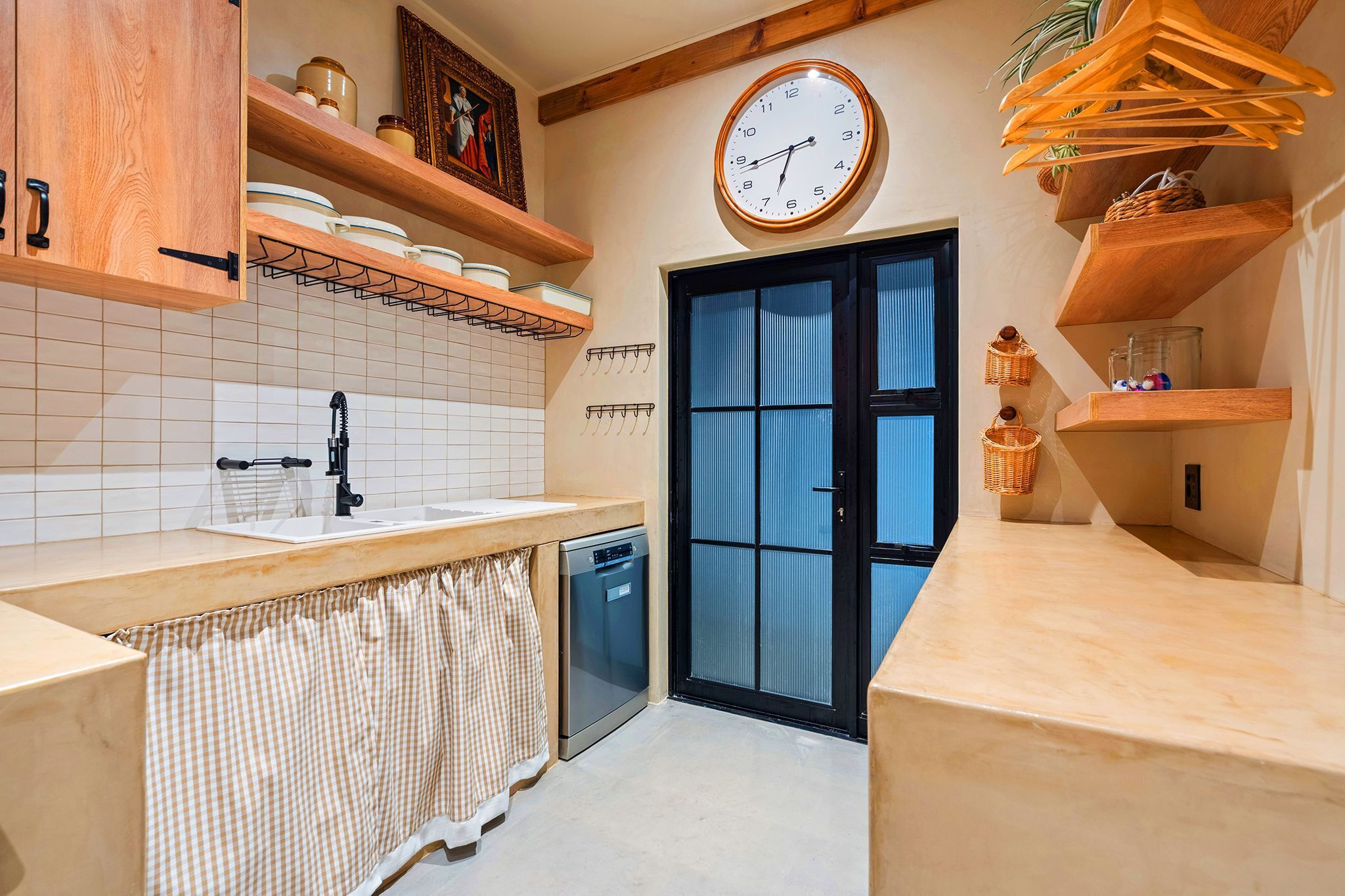 A kitchen with a sink, dishwasher, wooden cabinets, a clock, and a door with a window.