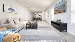A modern living room with a sofa, coffee table, and a TV mounted on the wall. - 4BR Pet-Friendly Beach Home | Walk to Beach & Jacksonville Beach Pier | Fenced Yard (Jacksonville Beach)