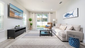 A modern living room with a sofa, coffee table, and a TV mounted on the wall. - 4BR Pet-Friendly Beach Home | Walk to Beach & Jacksonville Beach Pier | Fenced Yard (Jacksonville Beach)