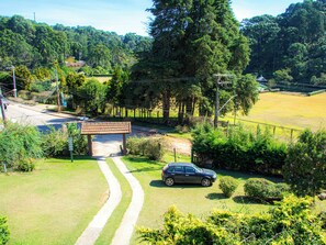 A rural landscape with a paved road, a car parked near a gazebo, and dense forest in the background. - Villa da Vila Montanhas (Monte Verde)