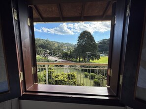 A view through a window with a wooden frame, a metal railing, and a clear sky. - Villa da Vila Montanhas (Monte Verde)