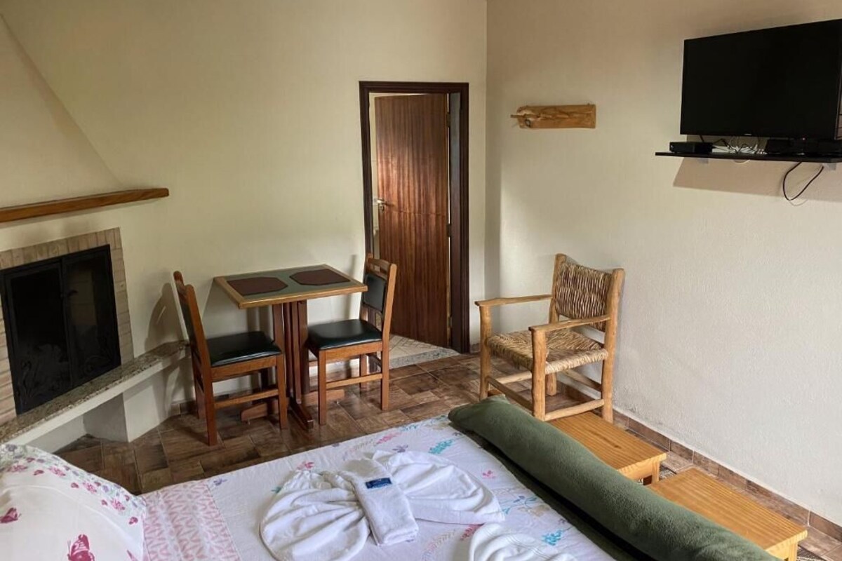 Una stanza con un letto, un tavolino con sedie, una televisione montata a parete e una sedia di legno.