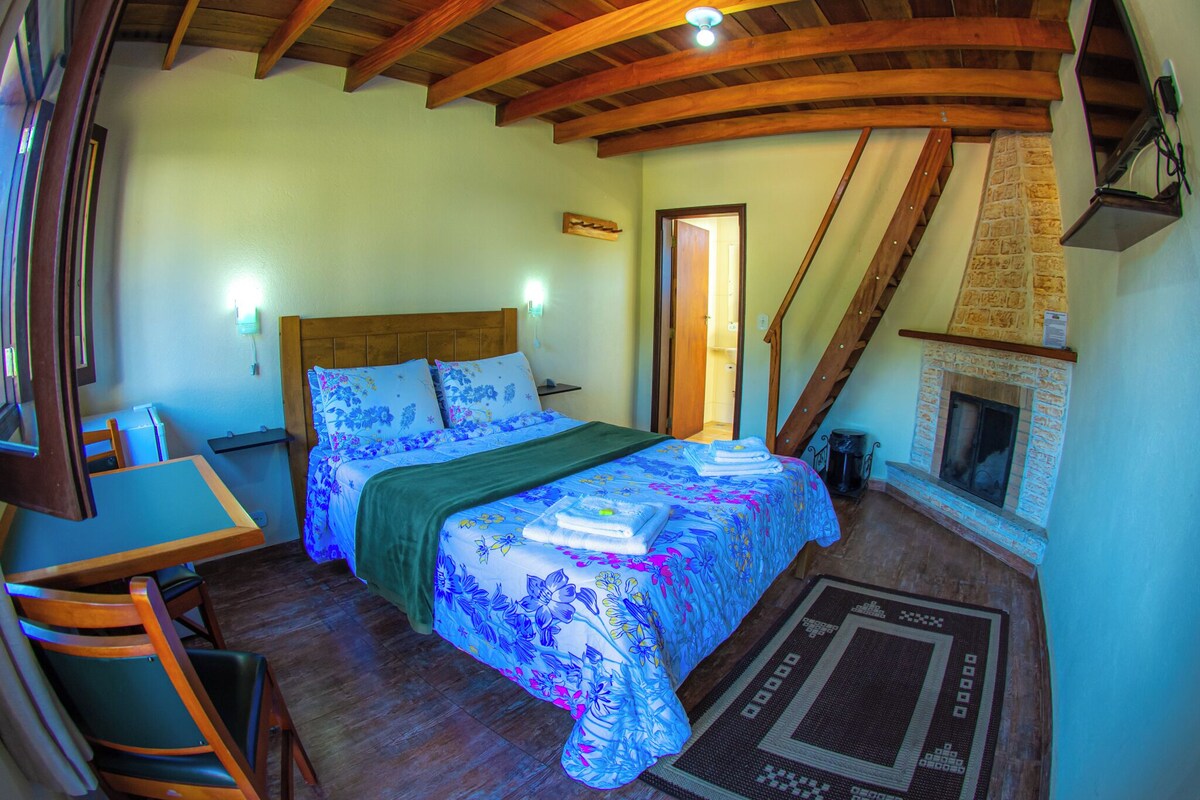 Camera da letto con soffitto in legno, un letto con biancheria a fiori, un camino e una scala.