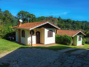 A two-story house with a tiled roof, a small porch, and a stone pathway leading to the entrance. - Villa da Vila Montanhas (Monte Verde)