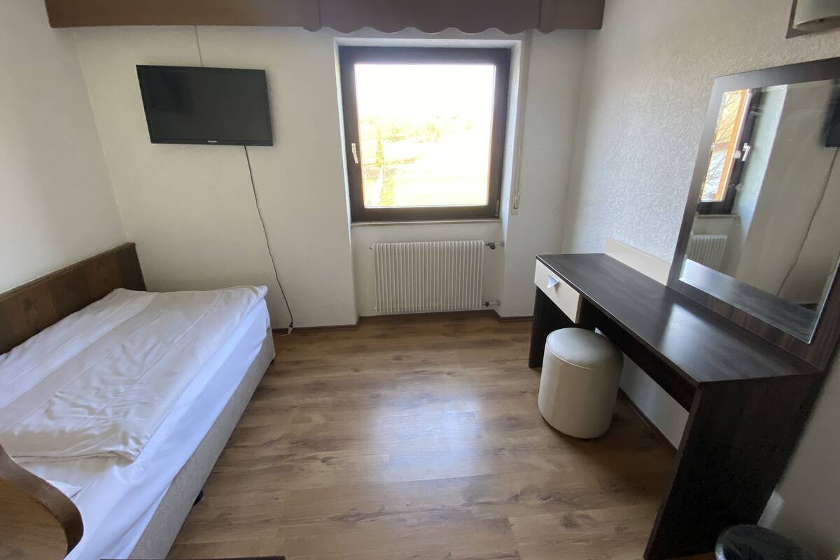 A bedroom with a bed, a desk, a chair, a radiator, and a TV.