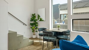Ein modernes Interieur mit einer Treppe, einem Esstisch mit Stühlen, einer großen Topfpflanze und Blick durch ein Fenster.