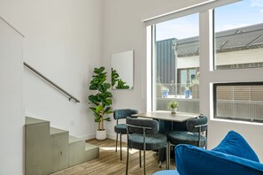 A modern interior with a staircase, a dining table with chairs, a large potted plant, and a view through a window. - Vibrant DT ATX Loft | Near Rainey St (Austin)