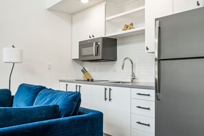 A modern kitchen with white cabinets, a stainless steel refrigerator, a microwave, and a sink. - Vibrant DT ATX Loft | Near Rainey St (Austin)