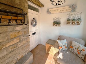 Une pièce chaleureuse avec un mur en pierre, une porte blanche, des meubles en osier et des œuvres d’art décoratives accrochées au mur.