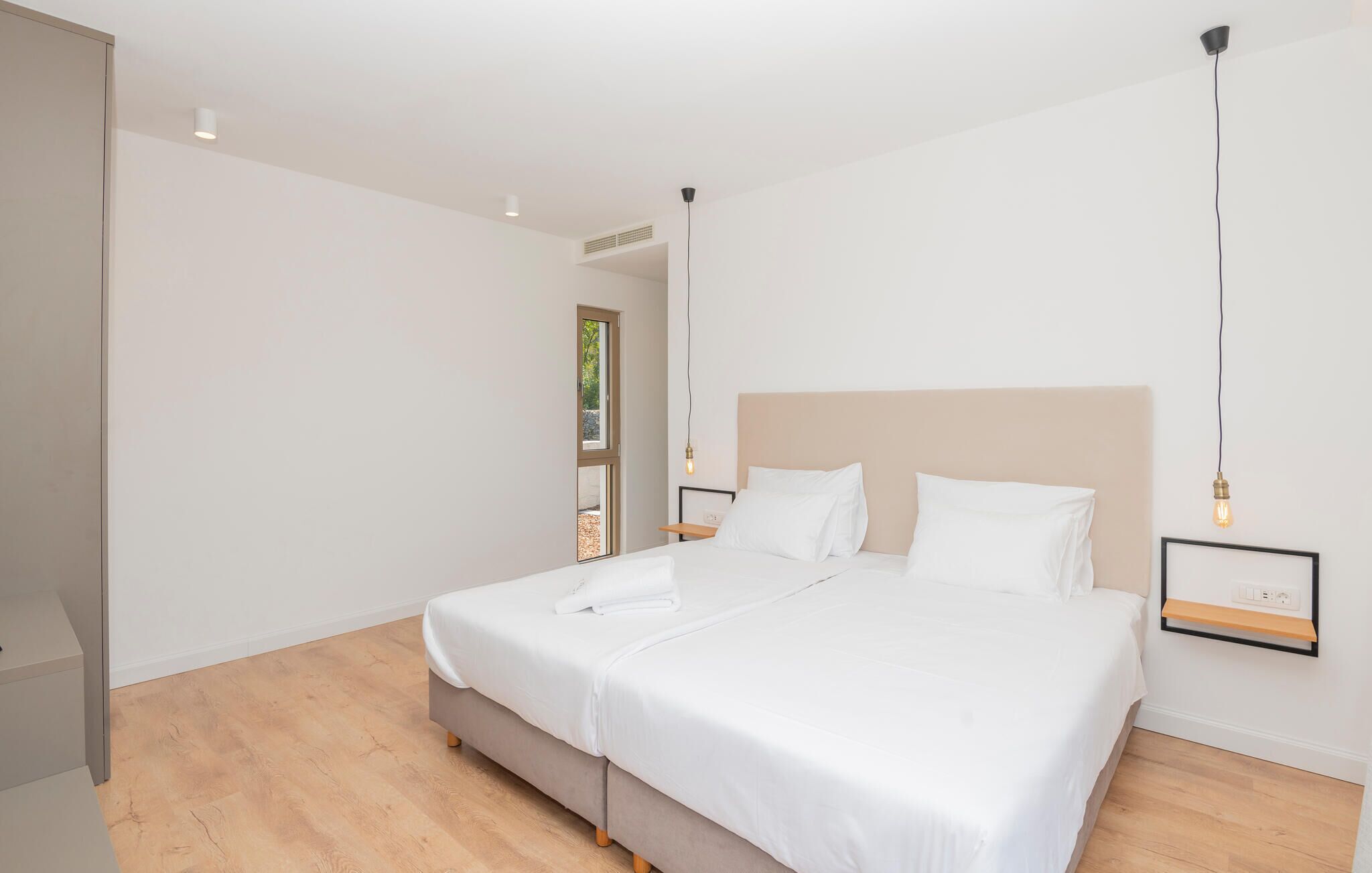 Ein modernes Schlafzimmer mit einem großen Bett, einem Kopfteil, Nachttischen und einem Fenster.