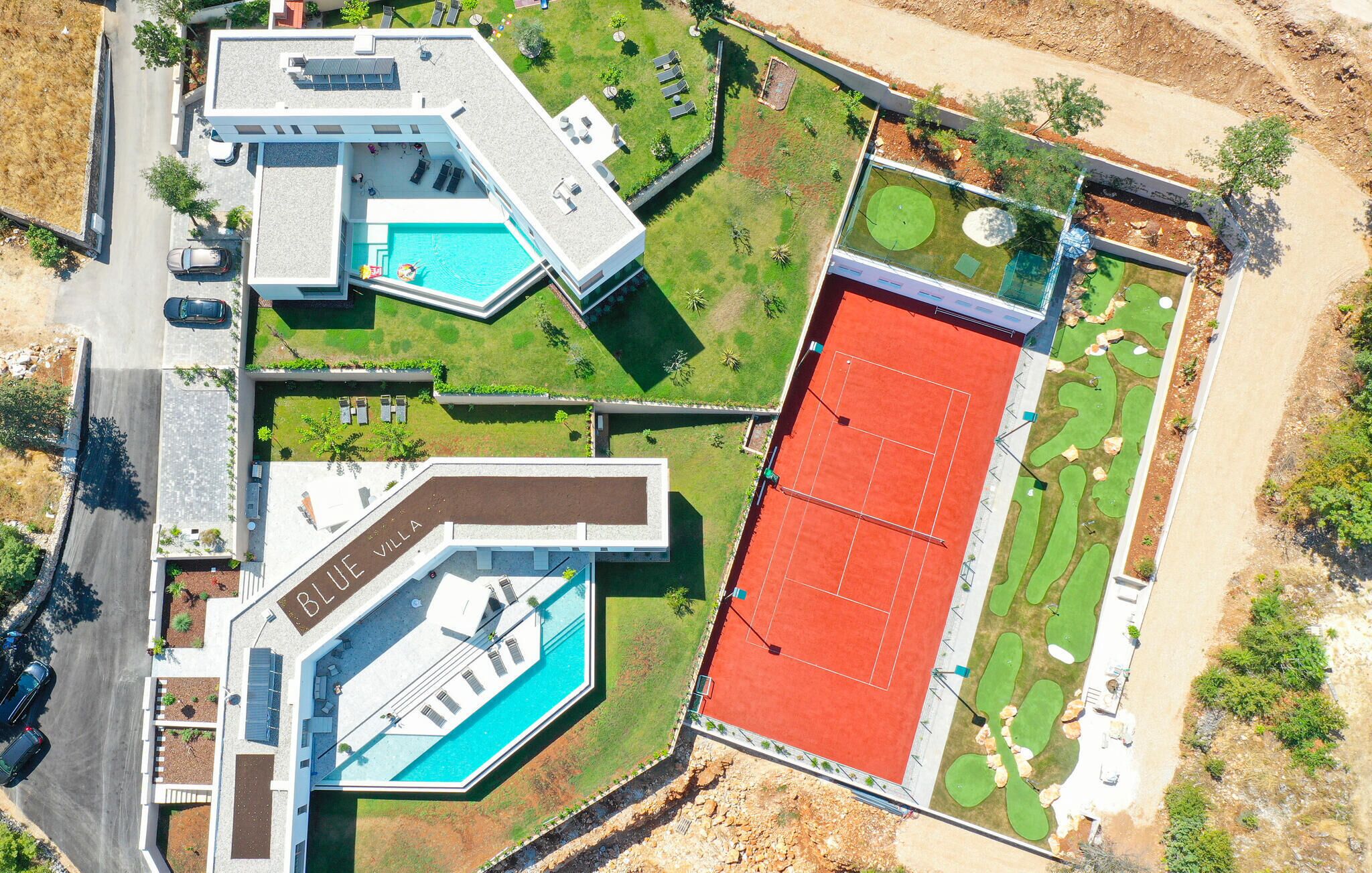 Vista aérea de una villa moderna con piscina, cancha de tenis y jardín ajardinado.