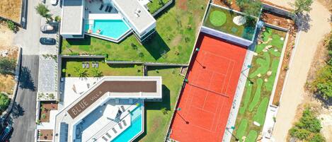 Vista aérea de una villa moderna con piscina, cancha de tenis y jardín ajardinado.