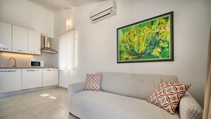 Ein modernes Wohnzimmer mit einer Couch, gemusterten Kissen, einem Gemälde und einer Küchenzeile mit Schränken und einer Mikrowelle.