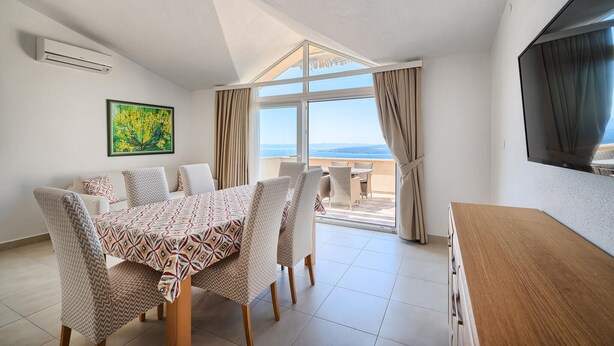 Ein Zimmer mit Esstisch, Stühlen, einem Gemälde, einer Klimaanlage, einem Fernseher und Meerblick.