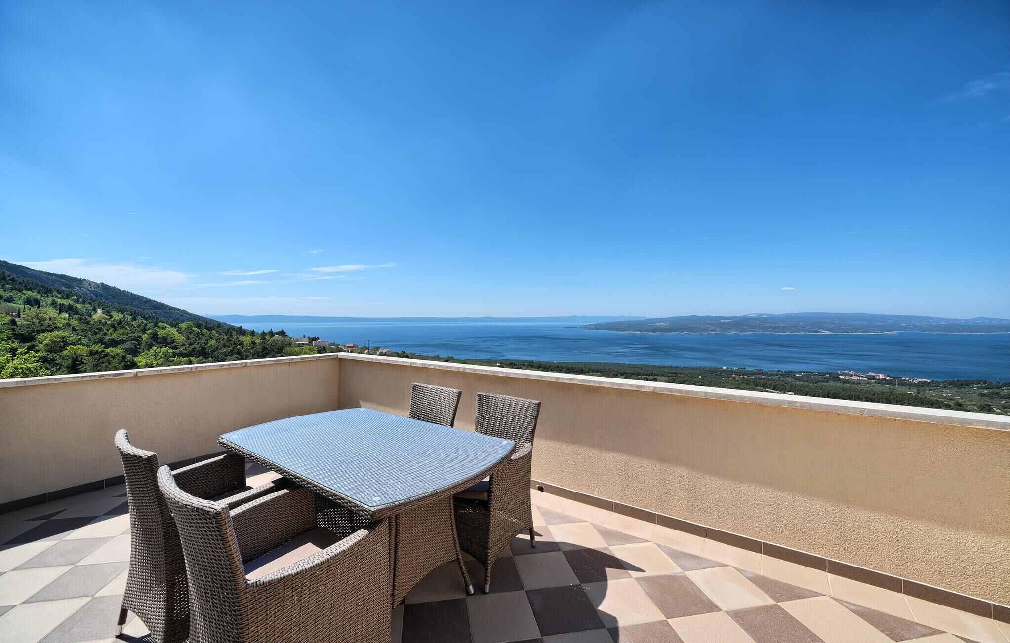 A balcony with a table and chairs, overlooking a coastal landscape.