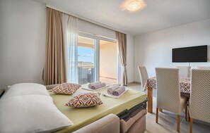 Ein Hotelzimmer mit Bett, Fernseher, Esstisch mit Stühlen und Blick durch eine Schiebetür.