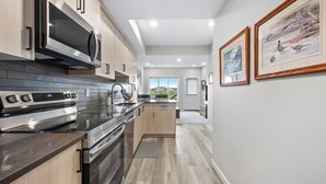 A modern kitchen with stainless steel appliances, wooden cabinets, and a view to the outdoors. - Mallard Cove | Pond Views | Pets Ok | Playground (Calgary)