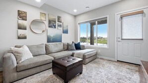 A living room with a sectional sofa, ottoman, and artwork on the walls. - Mallard Cove | Pond Views | Pets Ok | Playground (Calgary)