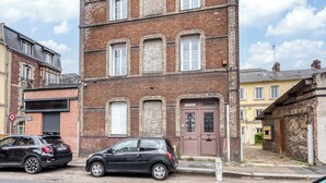 En byggnad i flera våningar, byggd av tegel, med en garageport på bottenvåningen, en svart bil parkerad framför och äldre byggnader intill.