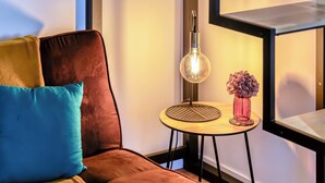 Ett modernt rum med en brun soffa, ett litet runt bord med en lampa och en vas med blommor.