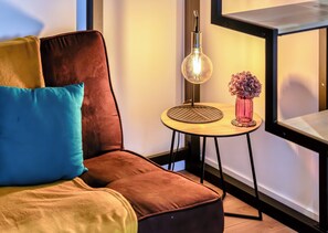 Una habitación moderna con un sofá marrón, una mesita redonda con una lámpara, y un florero con flores.